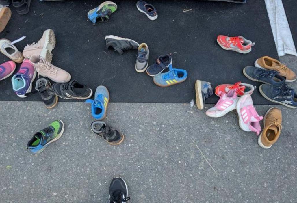 Lose auf dem Boden verstreute Paare von Kinderschuhen vor einer Hüpfburg.